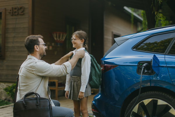 Portrait of a man charging his electric car in front of his house. The man is unplugging the charger from the fully charged car before driving daughter to school.