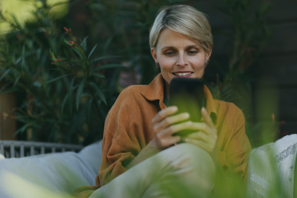 Beautiful woman relaxing in the garden, scrolling on her smartphone. Mother having a moment to herself while her child is sleeping