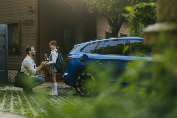 Father handing girl her science project, robotic arm for school science fair. Electric car is charging before going to school and work. Concept of young girls in science.