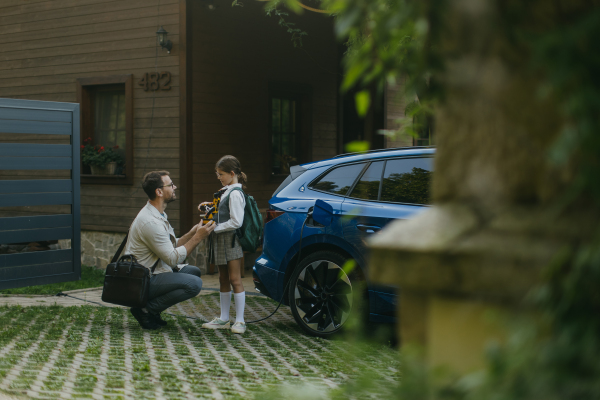 Father handing girl her science project, robotic arm for school science fair. Electric car is charging before going to school and work. Concept of young girls in science.