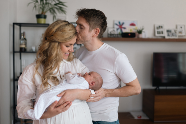 A smiling mother and father holding their newborn baby daughter at home