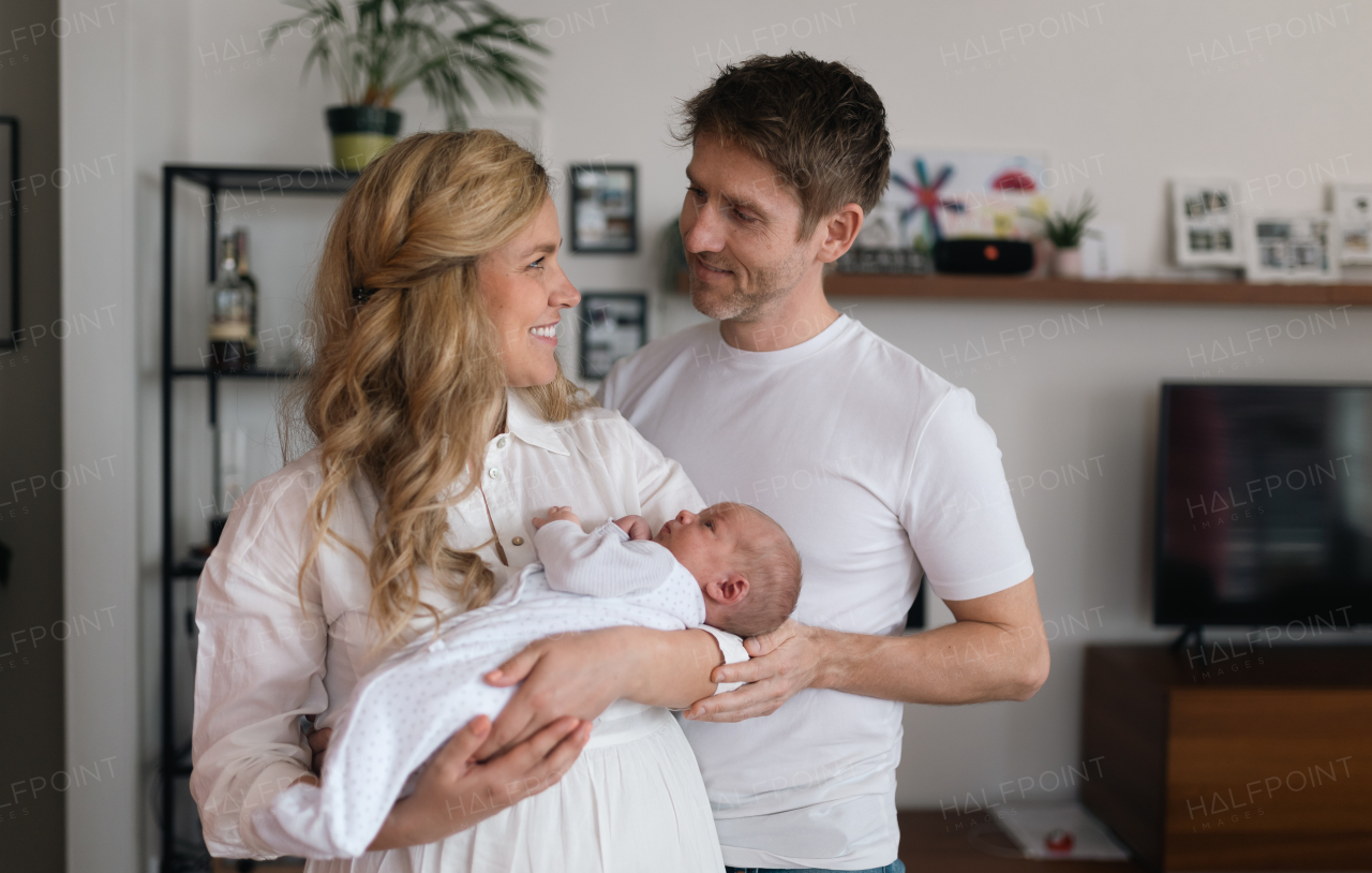 A smiling mother and father holding their newborn baby daughter at home