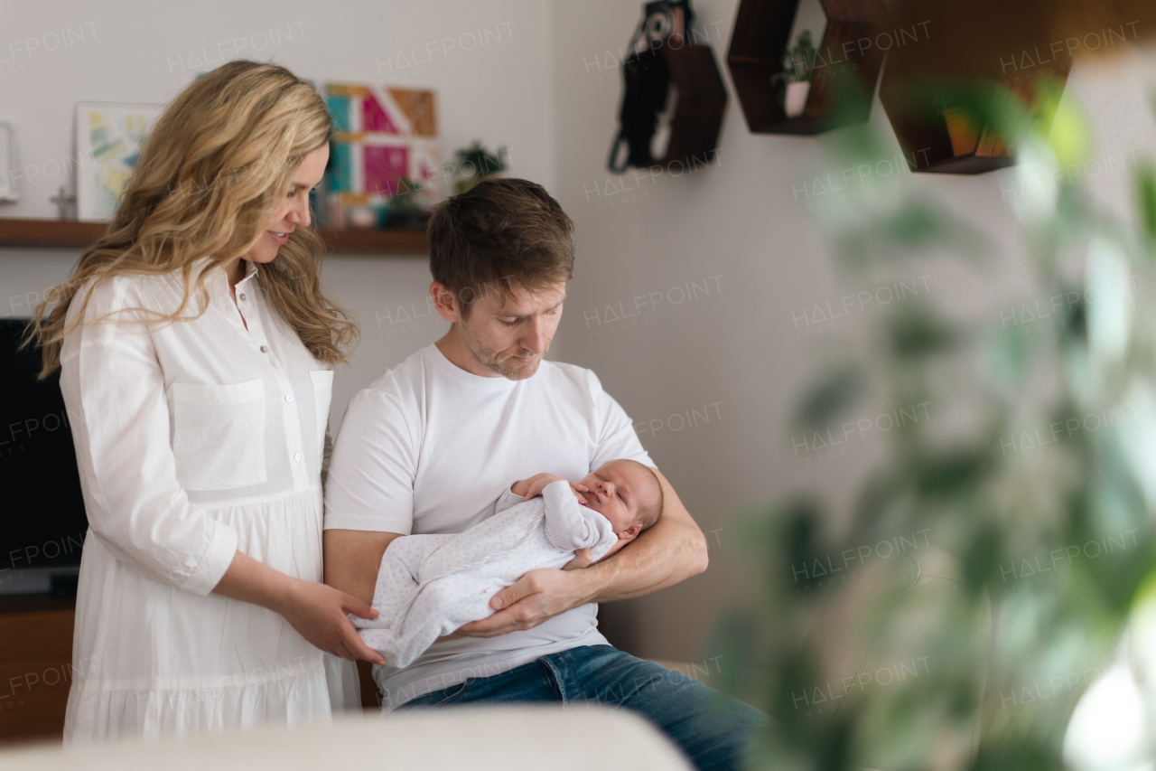 A smiling mother and father holding their newborn baby daughter at home