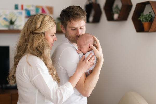 A smiling mother and father holding their newborn baby daughter at home