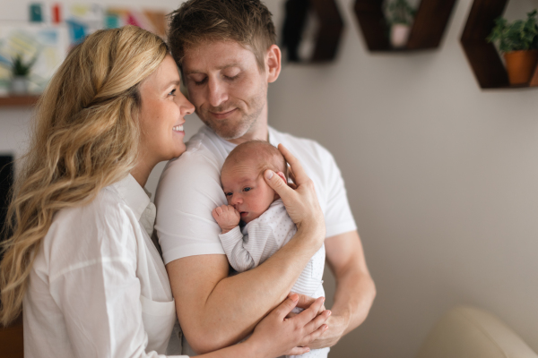 A smiling mother and father holding their newborn baby daughter at home