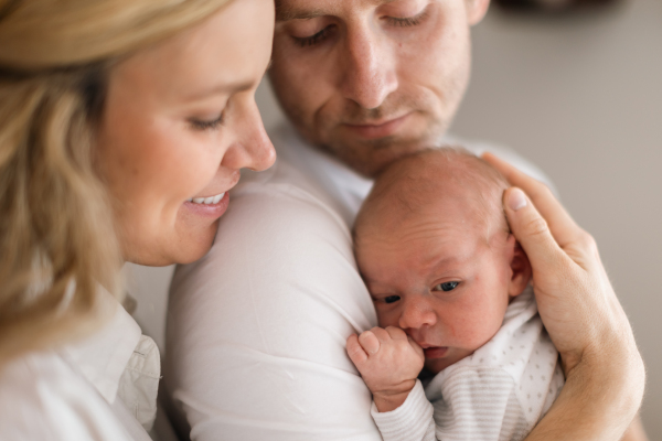 A smiling mother and father holding their newborn baby daughter at home