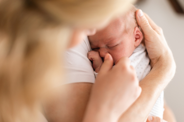 An unrecognizable mother holding her newborn son at home, close-up