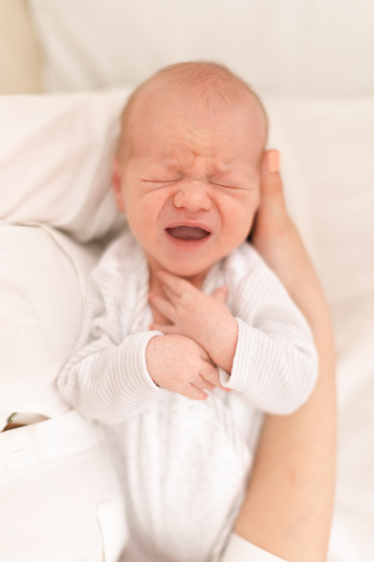 An unrecognizable mother holding her newborn son crying at home, close-up