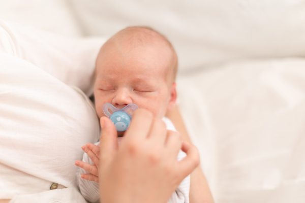 An unrecognizable mother holding her newborn son with dummy at home, close-up