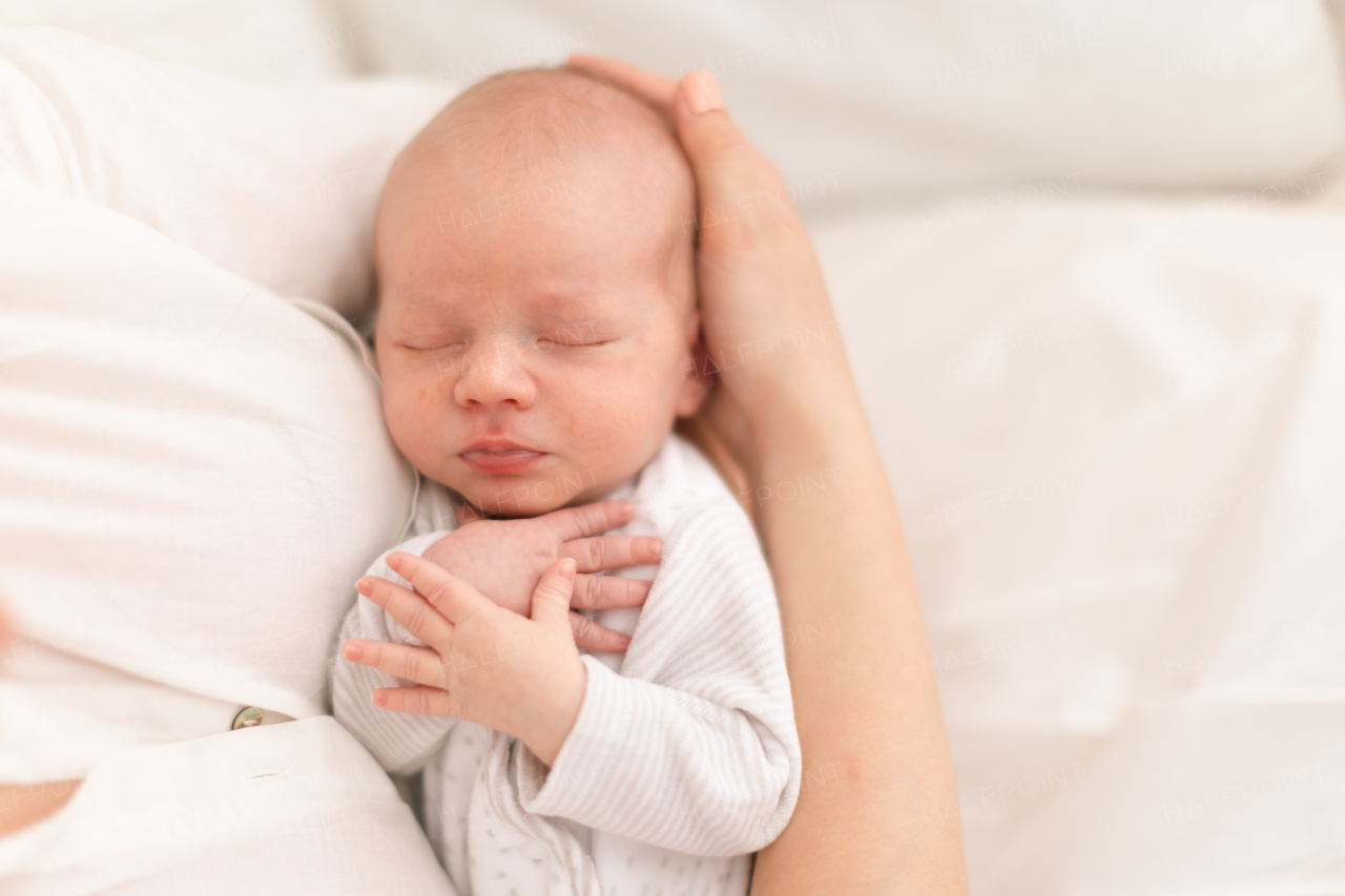 An unrecognizable mother holding her newborn son at home, close-up