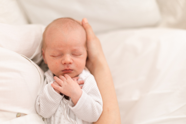 An unrecognizable mother holding her newborn son at home, close-up