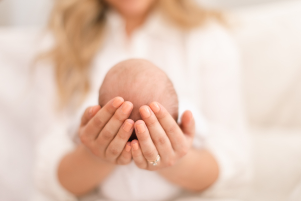 An unrecognizable mother holding her newborn son at home, close-up