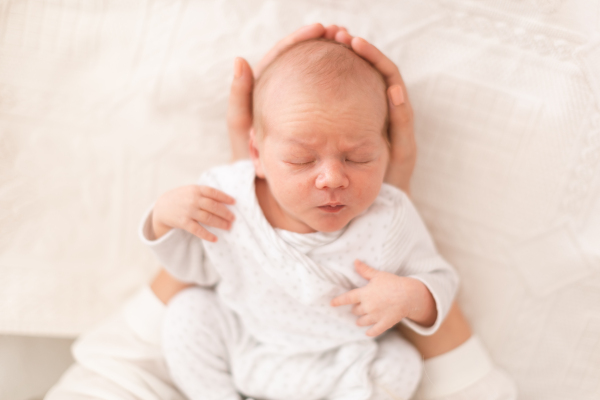 An unrecognizable mother holding her newborn son at home, close-up