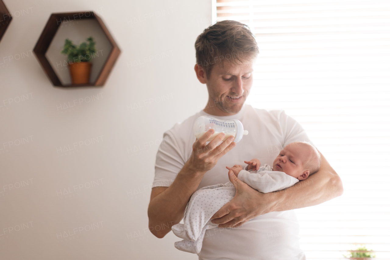 A father holding and feeding his newborn son with milk bottle at home.