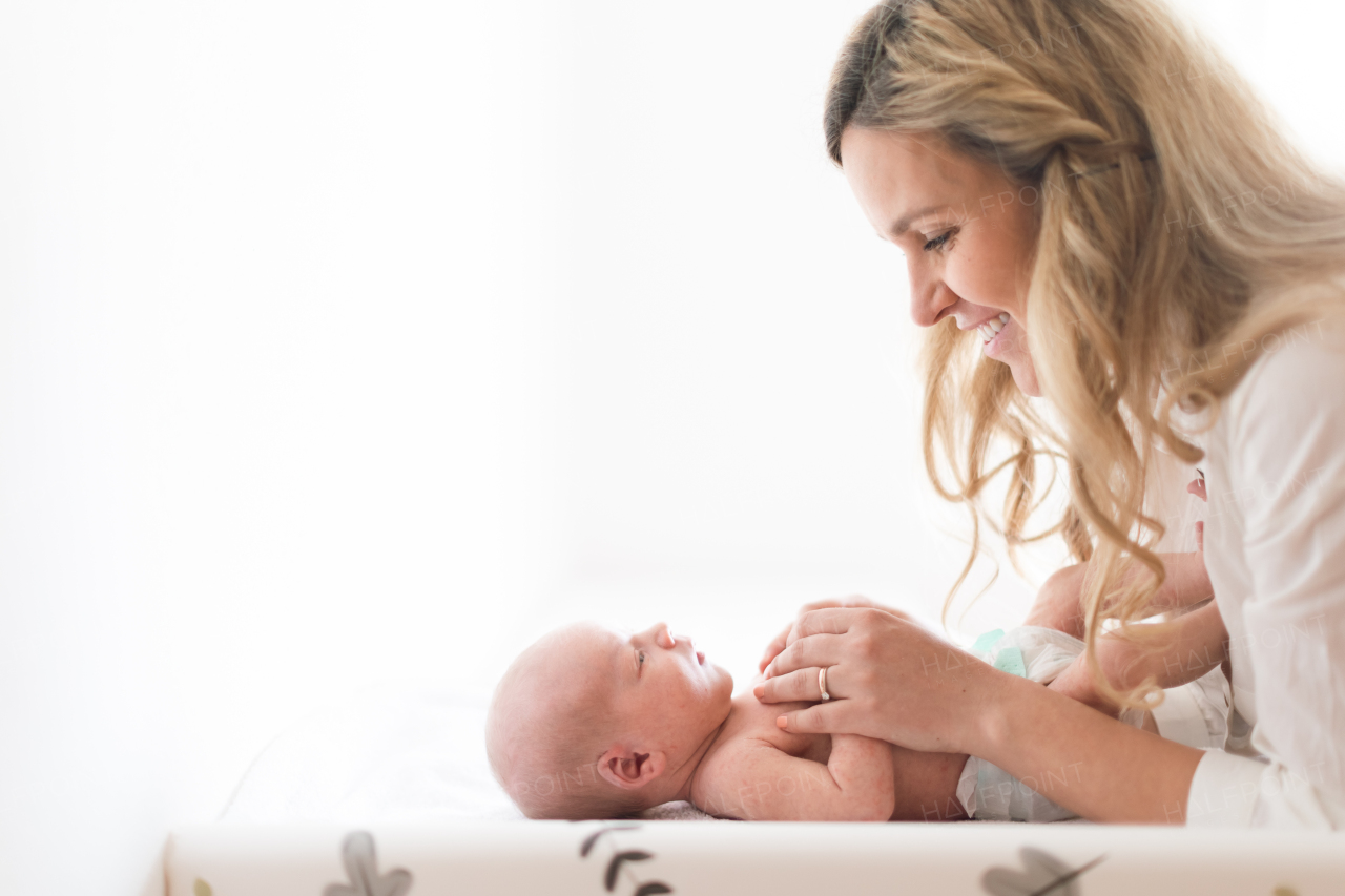 A happy mother bonding with her newborn son who is lying on changing mat at home.