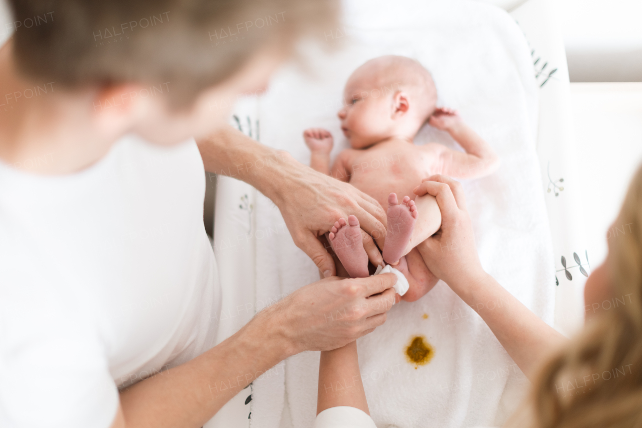 Parents together cahnging a nappy to newborn son who is lying on changing mat at home.