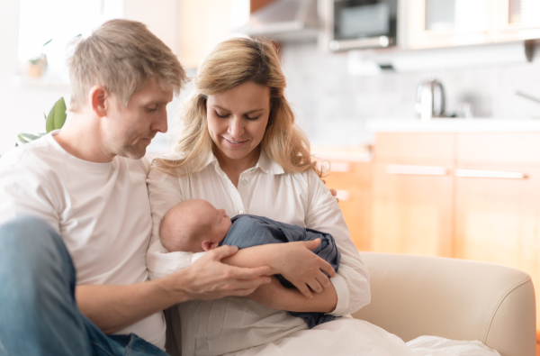 A smiling mother and father holding their newborn baby daughter at home