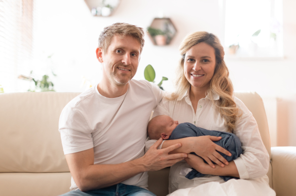 A smiling mother and father holding their newborn baby daughter at home