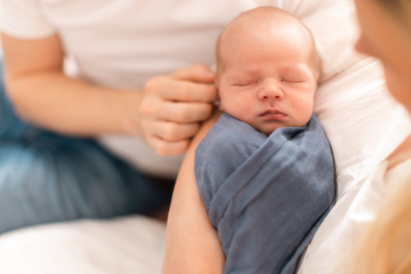 A close-up of parents holding neborn baby son wrapped in blanket at home.