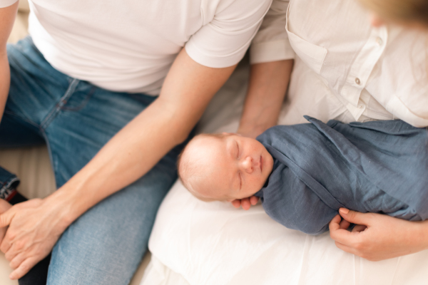 A close-up of parents holding newborn baby son wrapped in blanket at home.