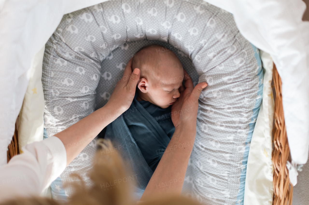 A newborn baby boy sleeping and swaddled in blue cloth lying in grey nest.