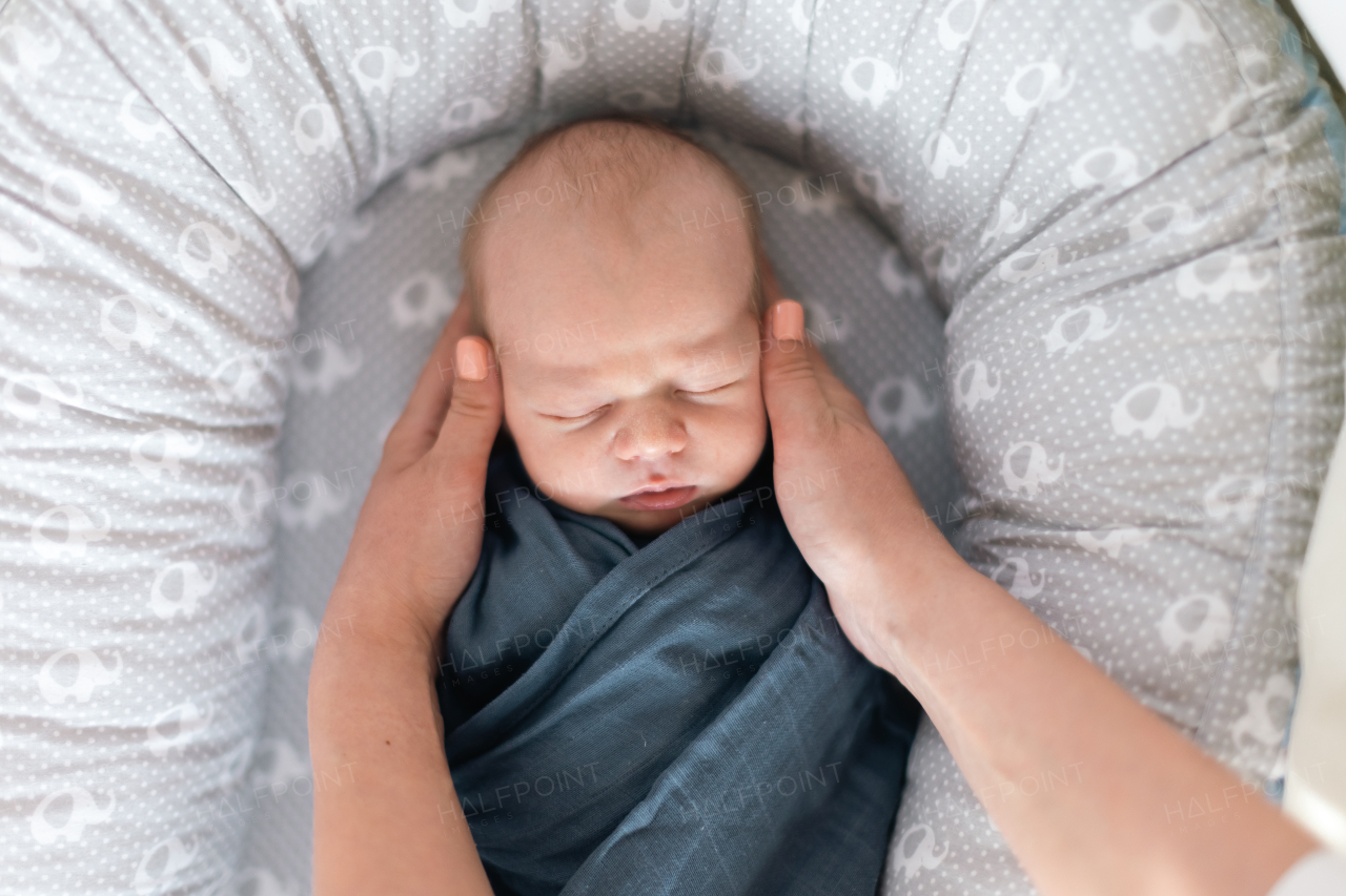 A newborn baby boy sleeping and swaddled in blue cloth lying in grey nest.