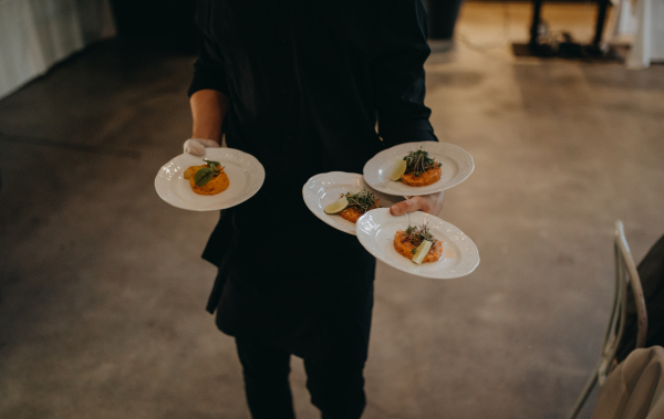 Waiter in black holding four plates with food in restaurant. Catering, service at the wedding reception. Salmon tartare as appetizer.