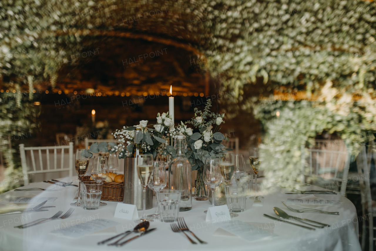 Elegant, romantic table setting for indoor wedding reception with fairy lights on brick wall behind. Luxury wedding table decoration, special event table set up with fresh flowers arragements.