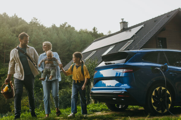 Family with electric car standing in front their house with solar panels on the roof. Solar energy and sustainable lifestyle of young family. Concept of green energy and sustainable future for next generations.