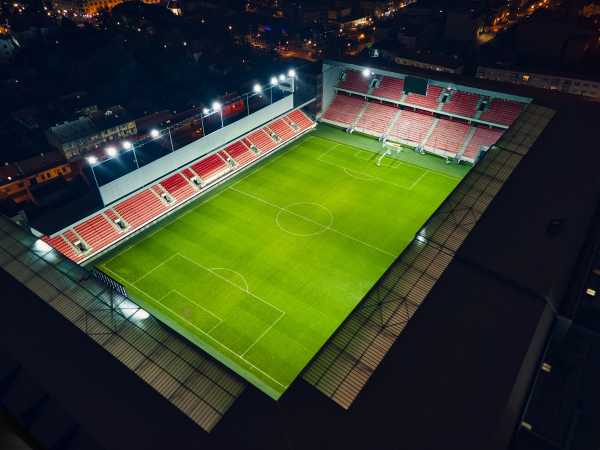 Aerial shot of an illuminated football stadium with an open roof at night. Football field with empty stands in city.