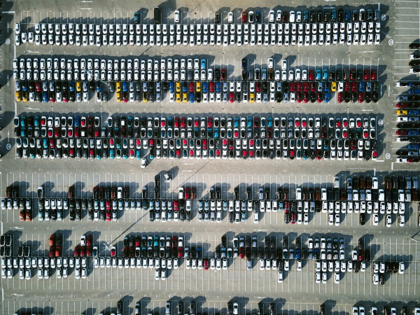 Aerial view of massive parking lot at a car manufacturing facility with newly produced vehicles parked in rows.