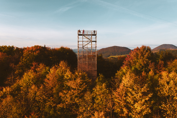 Aerial view of wooden lookout tower in autumn nature. People stand on the observation tower, enjoying beautiful, serene view of the surrounding landscape.