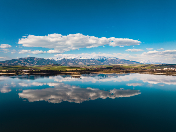 Aerial view from above the water surface of Liptovska Mara water reservoir on serene nature landscape, High Tatras Mountains in the distance.