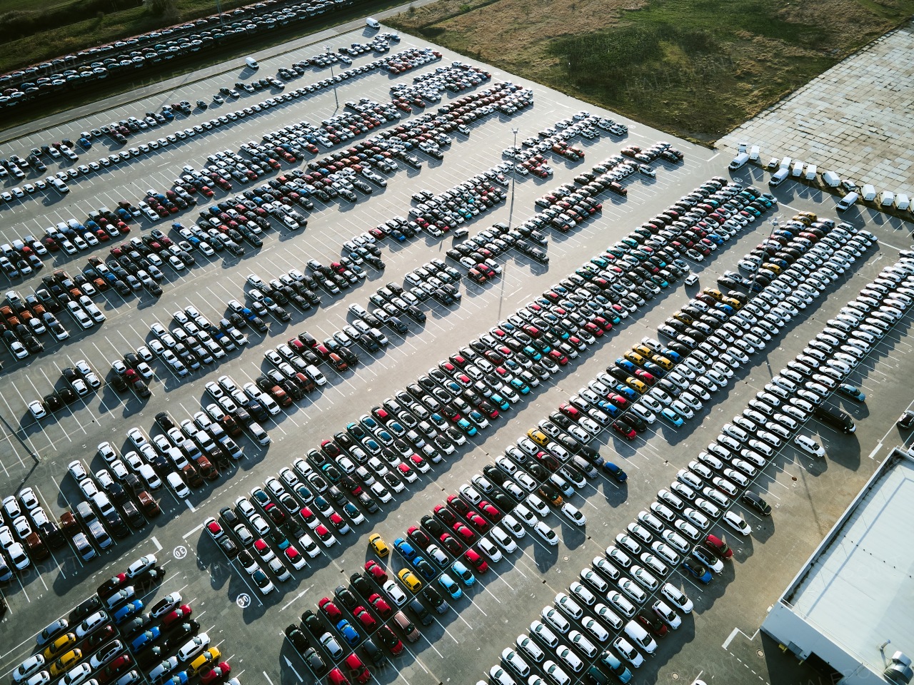 Aerial view of massive parking lot at a car manufacturing facility with newly produced vehicles parked in rows.