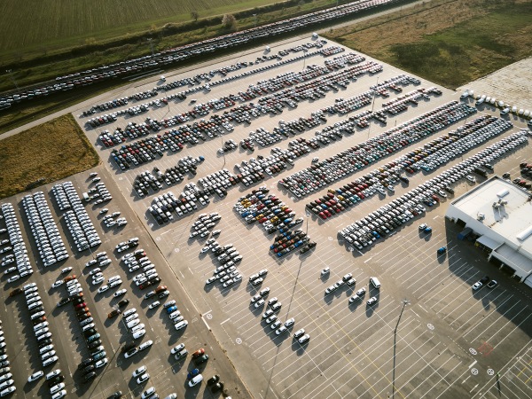 Aerial view of massive parking lot at a car manufacturing facility with newly produced vehicles parked in rows.