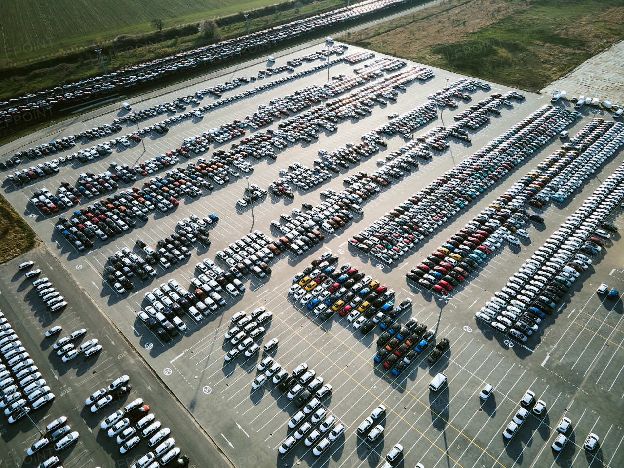 Aerial view of massive parking lot at a car manufacturing facility with newly produced vehicles parked in rows.