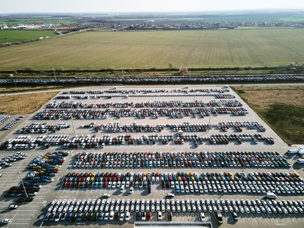 Aerial view of massive parking lot at a car manufacturing facility with newly produced vehicles parked in rows.