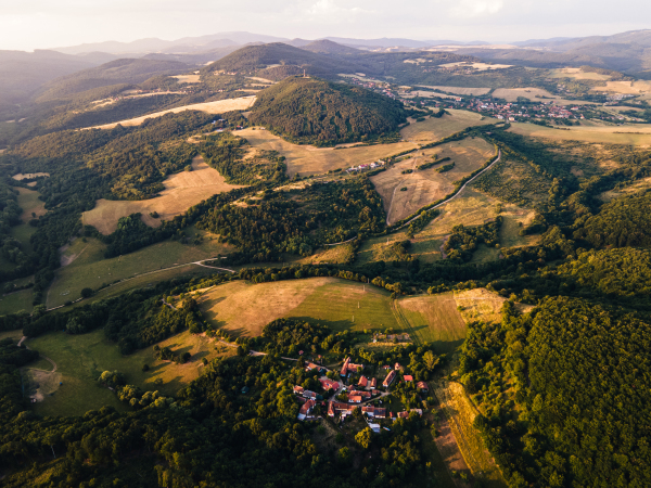 Aerial view of small village in the middle of green summer farm fields, crops or pasture with road and mountains.