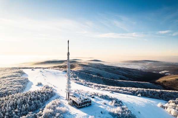 Aerial view of a transmitter, cell tower surrounded by a forest during winter. Drone view of snowy landscape, concept of the winter christmas holidays.