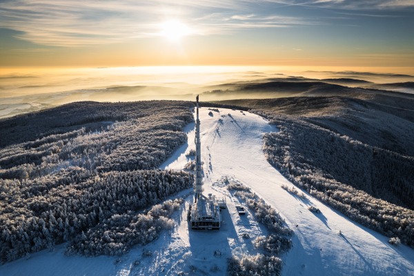 Aerial view of a transmitter, cell tower surrounded by a forest during winter. Drone view of snowy landscape, concept of the winter christmas holidays.