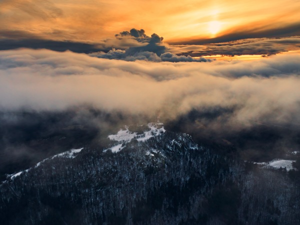 Aerial view of a transmitter, cell tower surrounded by clouds and the forest during winter. Drone view of snowy landscape, concept of the winter christmas holidays.