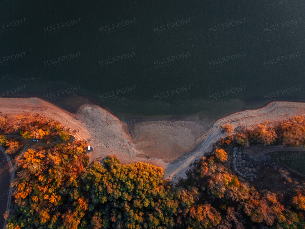 Top view of lake shore, surrounded by autumn forest with sand beach, coastline.