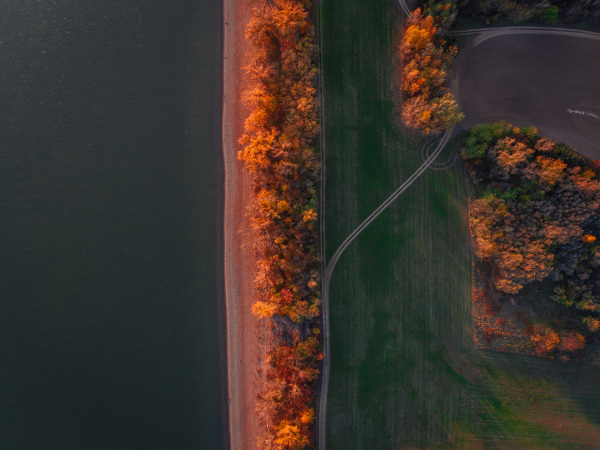 Top view of lake shore, surrounded by autumn forest with sand beach, coastline.