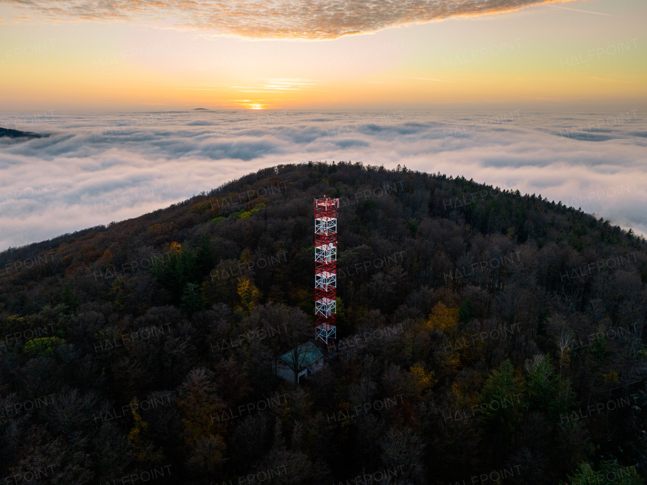 Aerial view of a transmitter, cell tower surrounded by a forest, clouds and fog. Drone view of landscape during sunset, sunrise.