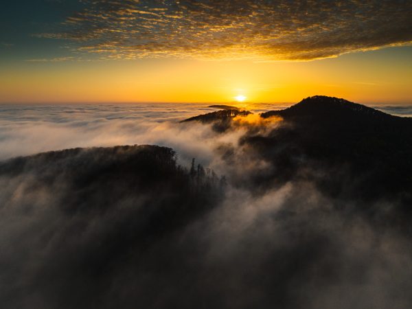 Mountains in low clouds at sunrise. Aerial view of beautiful landscape of mountain peak in fog during morning.