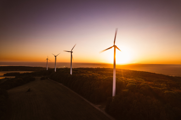 Aerial landscape photography of sunrise over nature with wind turbines. Wind turbine towers in soft morning light with forest, trees around, harmony of nature and technology. Concept of wind power as clean, renewable energy source.