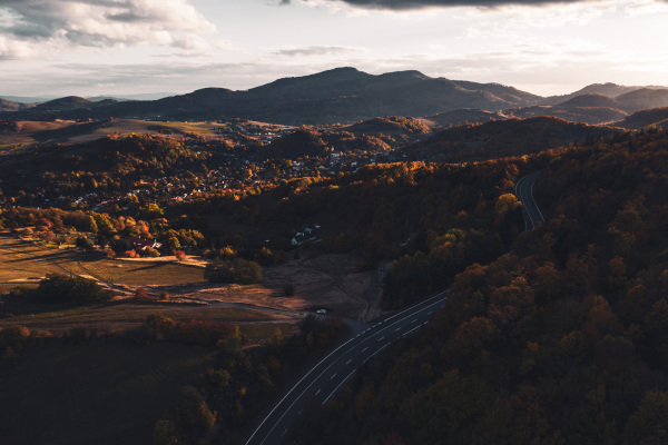 Aerial view of a autumn forest with road in the middle of trees. Winding mountain road inside colorful fall forest.