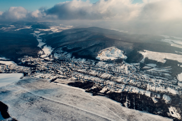 Aerial view of a small village surrounded by a forest during winter. Drone view of snowy landscape, concept of the winter christmas holidays.