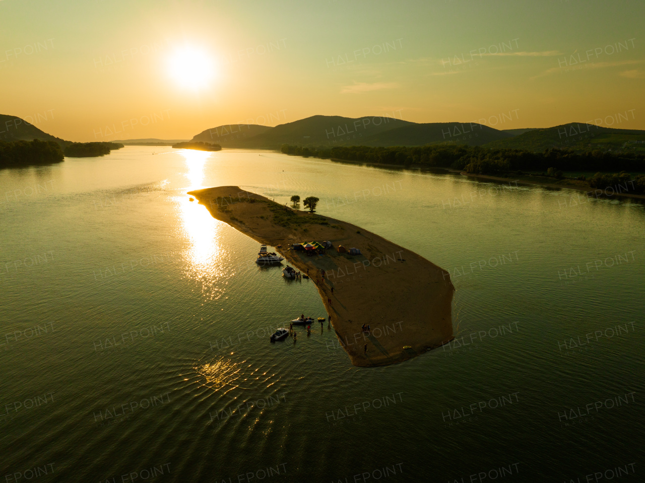 Top view of small river island, surrounded by water during warm summer sunset. Camping on riverine or lake island.