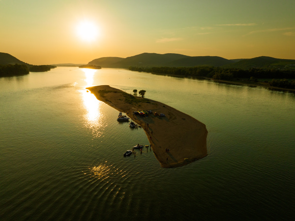 Top view of small river island, surrounded by water during warm summer sunset. Camping on riverine or lake island.